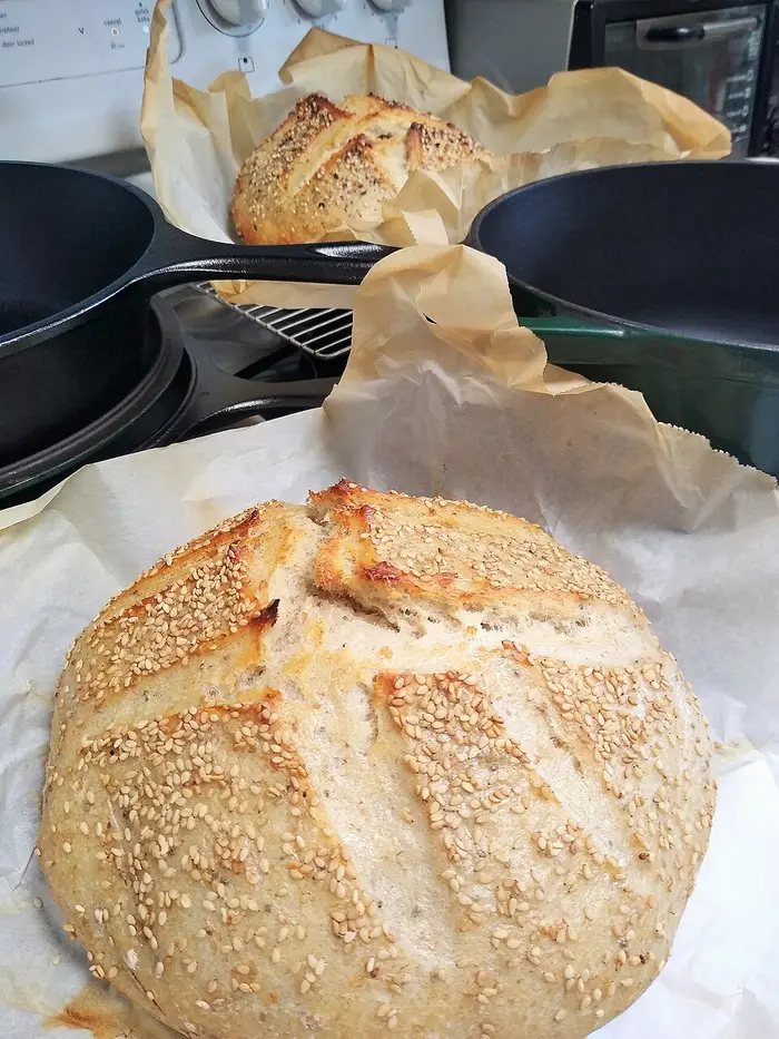 Freshly baked loaves resting on parchment beside their Dutch ovens