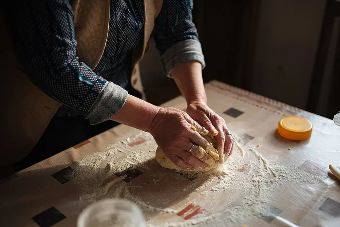 Hands kneading bread dough on a floured wooden table