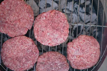 Seasoned beef patties grilling on a charcoal grate