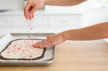Scatter the crushed candy canes evenly over the wet white chocolate and press down very lightly with your palm so the pieces stick.